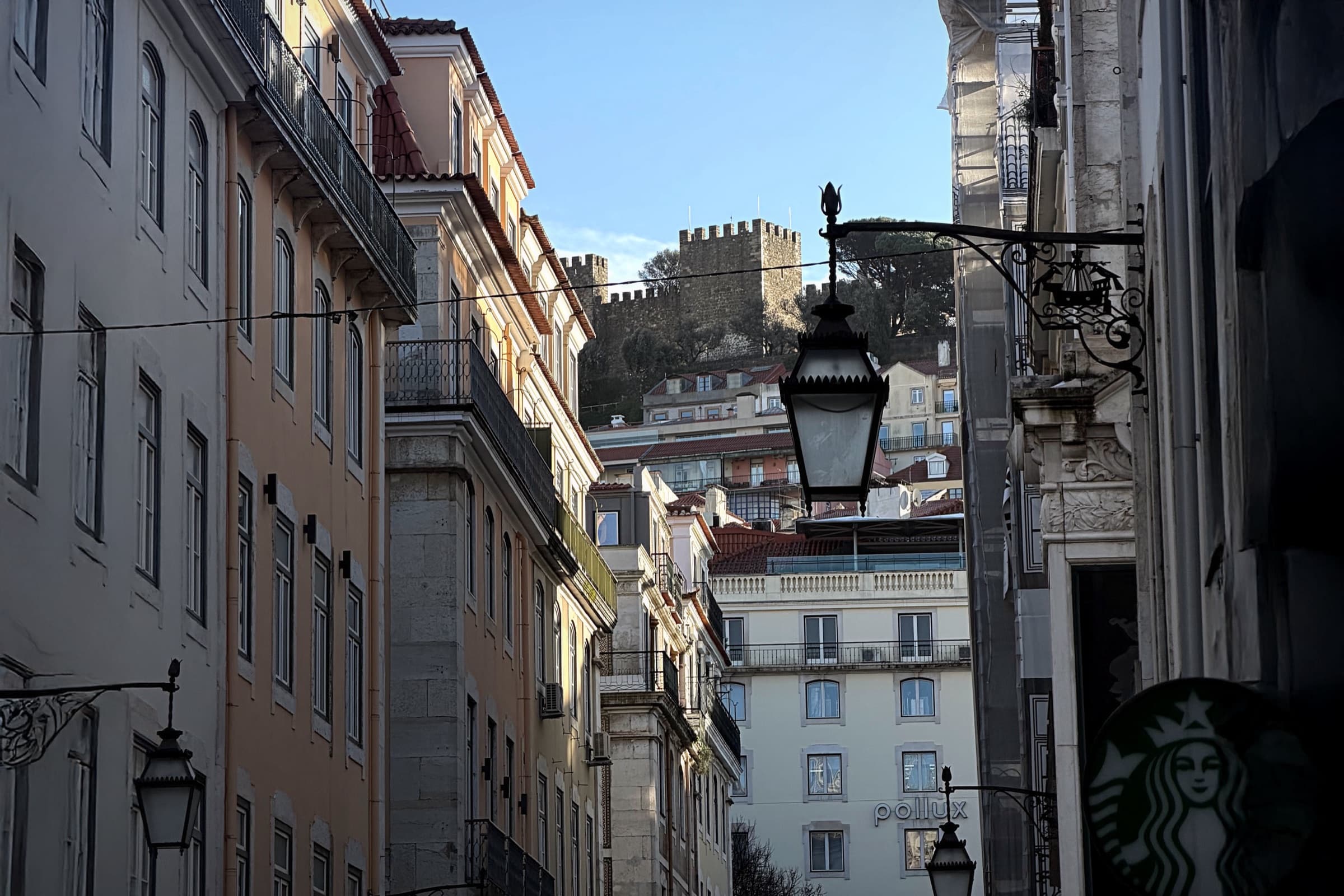 A narrow Lisbon street with a historic facade, street lamps, and a visible Starbucks sign.