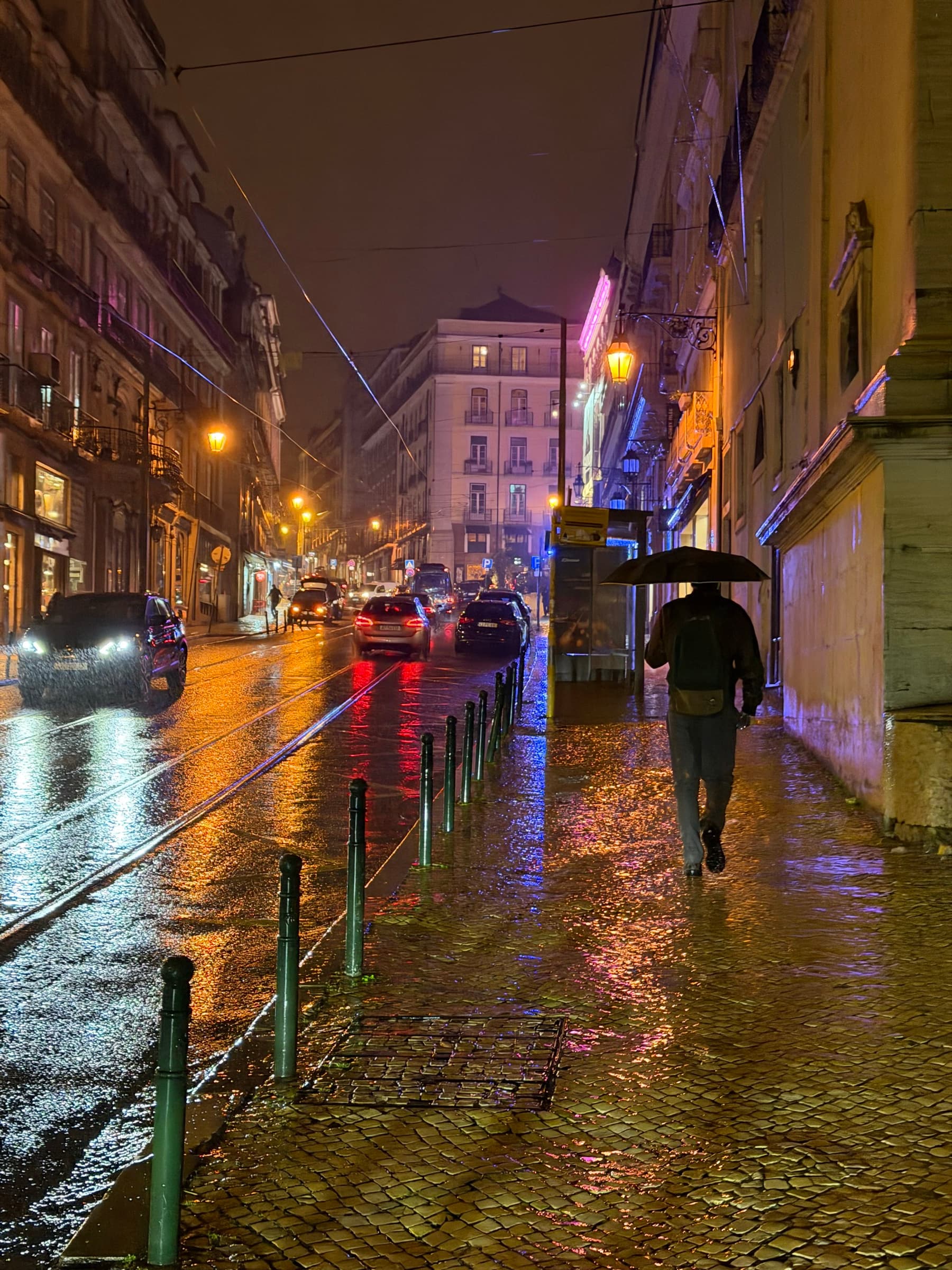 A Lisbon street at night with neon light and wet pavement dissolving into reflections.