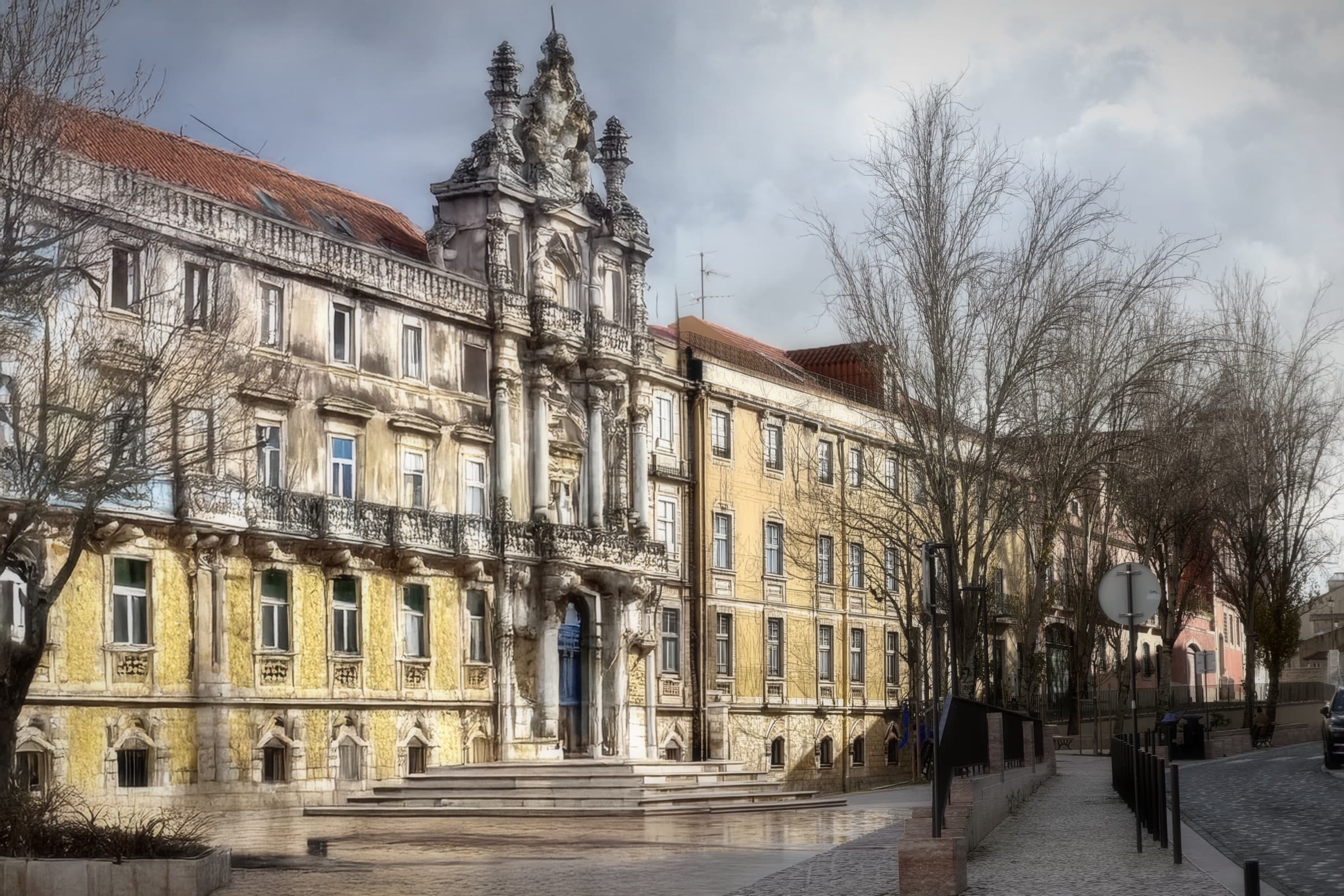 A yellow Lisbon facade and church tower seen through bare trees on a quiet street.